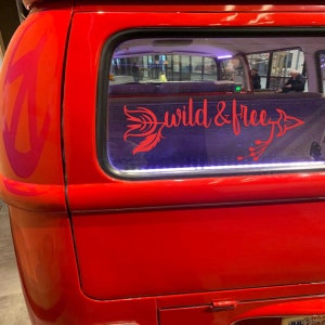 May include: A red vintage van with a rear window decal that reads "wild & free" with an arrow and feather design.