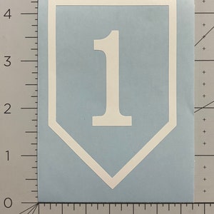 May include: White vinyl decal of a white shield with a white number 1 inside. The shield is a traditional military style.