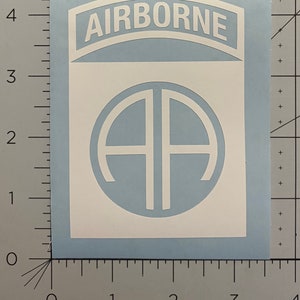 May include: White vinyl sticker with a blue background. The sticker features a white circle with the letters "AA" inside. Above the circle is a white curved banner with the word "AIRBORNE" in white letters.