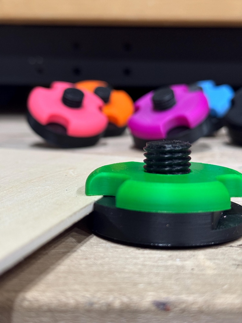 May include: A close-up shot of several colorful, plastic, screw-on knobs. The knobs are in various colors, including pink, orange, purple, and green. Each knob has a black base and a black screw.