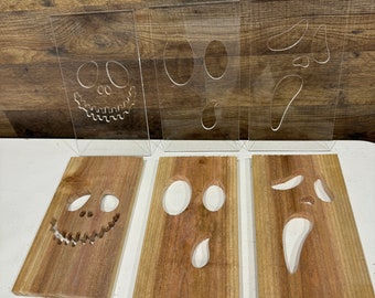 Könnte beinhalten: Drei Halloween-Holztafeln mit ausgeschnitzten Gesichtern, jeweils gepaart mit einer transparenten Acrylauflage mit passenden Designs. Die Holztafeln sind rechteckig und haben eine natürliche Holzmaserung.