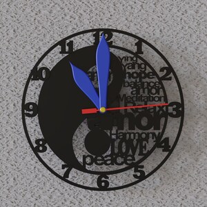 May include: A black Yin and Yang wall clock with blue hands and a red second hand. The clock face features the numbers 1-12, and words like "hope", "love", and "peace". The clock is mounted on a textured gray wall.