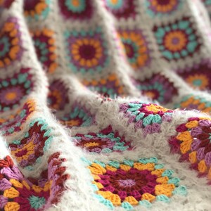 Könnte beinhalten: Eine gehäkelte Decke mit einem Granny-Square-Muster in den Farben Weiß, Rosa, Gelb und Blau.