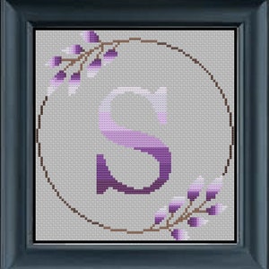 Puede incluir: Un patrón de punto de cruz con la letra "S" en un diseño degradado de morado, rodeado de una corona marrón con hojas moradas.