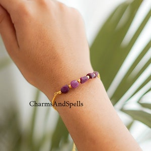 May include: A purple gemstone bracelet with gold accents. The bracelet is made with small, rectangular-shaped gemstones and a delicate gold chain.