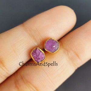 Puede incluir: Un par de pendientes de oro con piedras preciosas de rubí rosa. Los pendientes tienen un estilo simple y moderno.