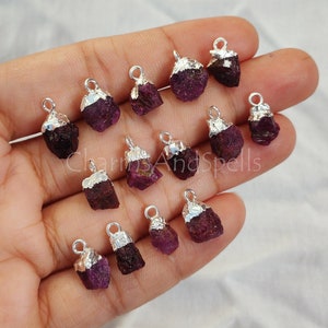 May include: A collection of 14 raw ruby gemstone pendants with silver-plated bail settings. The ruby stones are a deep red color and have a natural, rough texture. The pendants are perfect for jewelry making or crafting.