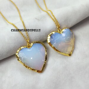 May include: Two gold necklaces with opal heart pendants. The hearts are a light blue color with a gold rim. The necklaces are on a white background.