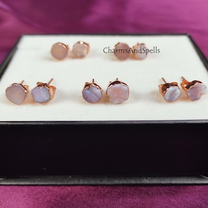 May include: A set of six rose gold earrings with irregular shaped white and pink stones. The earrings are displayed in a white box with the text "CharmsAndSpells" printed on the top.