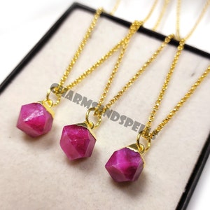 Peut inclure: Trois colliers dorés avec des pendentifs en pierres précieuses rose vif et facettées. Les pendentifs hexagonaux ont des capuchons dorés. Les colliers sont présentés dans une boîte noire.