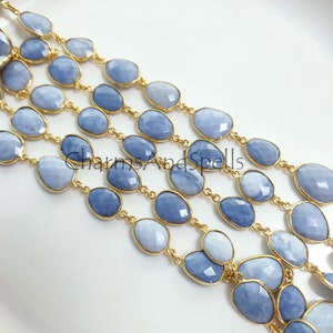 May include: A strand of blue gemstone beads with gold chain links. The beads are oval shaped and have a faceted finish. The chain is delicate and has a polished gold finish.