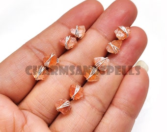 May include: A set of six raw, orange sunstone earrings. Each earring is wrapped in silver wire and has a natural, irregular shape.
