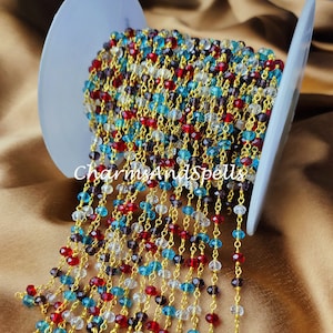 May include: A spool of gold chain with faceted glass beads in red, clear, blue, and purple. The chain is strung with alternating beads and is ready to be used for jewellery making.