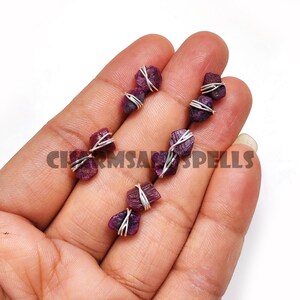 May include: Six small, raw ruby crystals wrapped in silver wire. The crystals are a deep red colour and have a natural, irregular shape.
