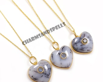 May include: Three heart-shaped pendants with gold chains. The pendants are white with gray veining and a small, round, blue stone in the center. The pendants are on a white background. The text "CHARMSANDSPELLS" is visible.