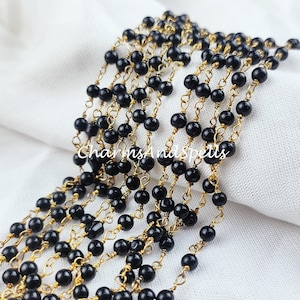 May include: A black bead and gold chain necklace. The chain is made of small, delicate links. The beads are round and smooth.