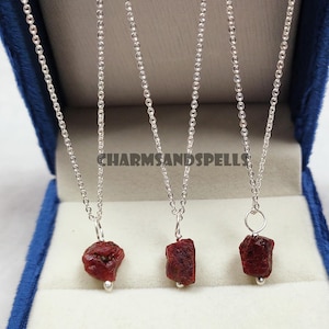 May include: Three silver necklaces with red gemstone pendants. The necklaces are displayed in a blue velvet box. The pendants are rough, natural stones.