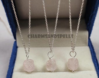 May include: Three silver necklaces with pink rose quartz pendants. The necklaces are displayed in a blue velvet box.