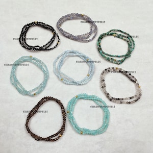 May include: Assortment of eight gemstone bracelets with gold accents. The bracelets are made with various colors of gemstones, including black, gray, blue, green, and brown.