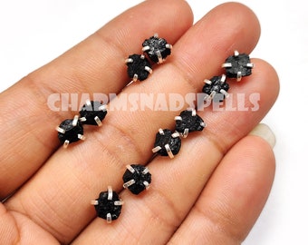 May include: Six black raw gemstone earrings with silver settings. The earrings are displayed on a hand.