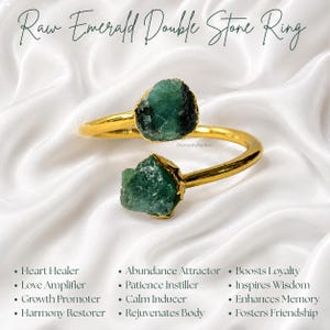 Peut inclure: Une bague ouverte dorée avec deux pierres d'émeraude brutes et non taillées à chaque extrémité. Le texte "Raw Emerald Double Stone Ring" figure en haut, accompagné d'une liste d'attributs comme "Heart Healer" et "Abundance Attractor".