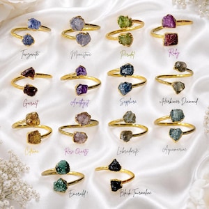 Peut inclure: Une collection de quatorze bagues ouvertes dorées, chacune ornée de deux pierres précieuses brutes et non taillées. Les pierres incluent tanzanite, pierre de lune, péridot, rubis, grenat, améthyste, saphir, diamant herkimer, citrine, quartz rose, labradorite, aigue-marine, émeraude et tourmaline noire.
