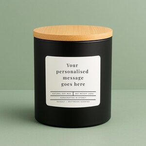 May include: A black candle with a wooden lid. The label reads "Your personalised message goes here". The candle is labeled "Natural Soy Wax" and "Seasalt + Driftwood Scented". Net weight is 260g. Handcrafted in Sydney.