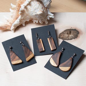May include: Three pairs of wooden earrings displayed on black card stock. The earrings are made of different shapes and wood grain patterns.