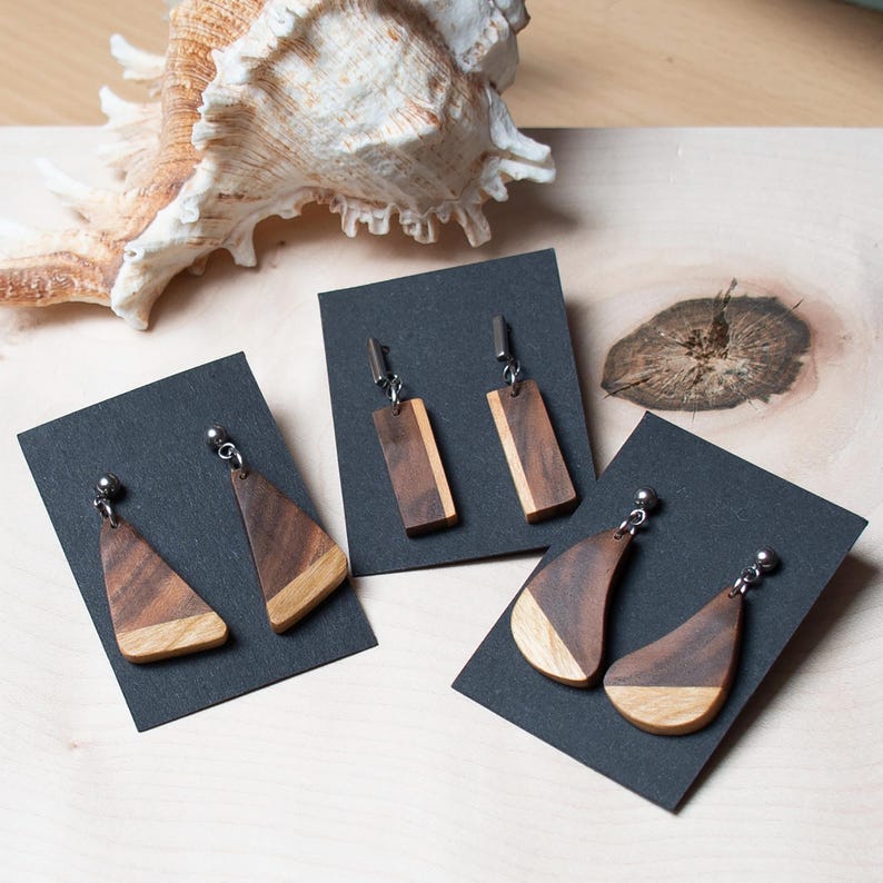 May include: Three pairs of wooden earrings displayed on black card stock. The earrings are made of different shapes and wood grain patterns.