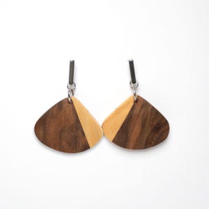 May include: A pair of wooden earrings with a light brown and dark brown wood design. The earrings are shaped like a teardrop and have a silver hook.