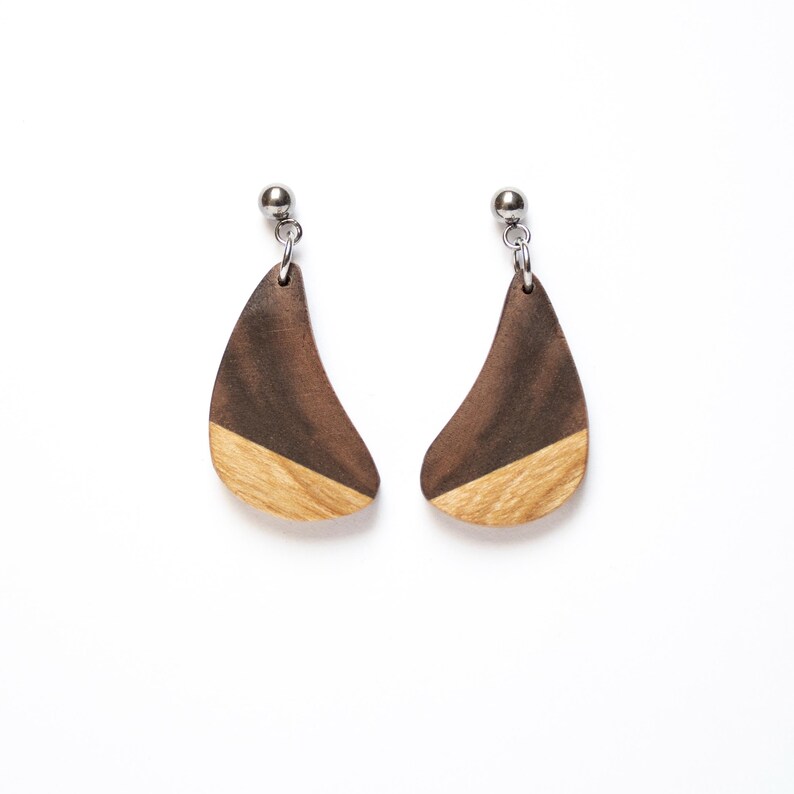 May include: A pair of wooden earrings with a dark brown and light brown wood design. The earrings are shaped like a teardrop and have a silver metal hook.
