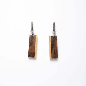 May include: A pair of wooden earrings with a dark brown and light brown wood pattern. The earrings are rectangular in shape and have silver metal hooks.