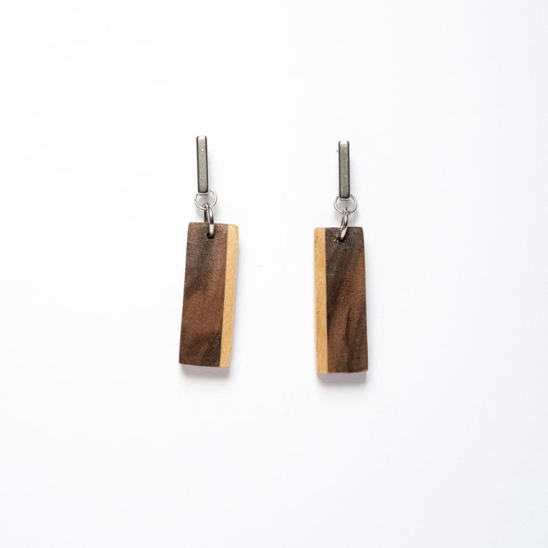 May include: A pair of wooden earrings with a dark brown and light brown wood pattern. The earrings are rectangular in shape and have silver metal hooks.