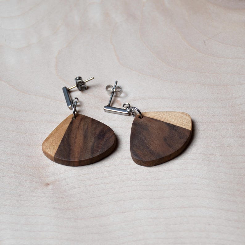 May include: A pair of wooden earrings with a teardrop shape. The earrings are made of two different types of wood, one light and one dark. The earrings are attached to silver posts.
