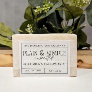 Puede incluir: Una barra de jabón blanca de leche de cabra y sebo con una etiqueta que dice "The Dancing Sun Company Plain & Simple unscented Goat Milk & Tallow Soap All Natural 4.5-4.75 oz"