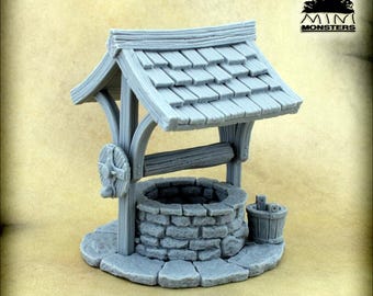 Puede incluir: Un pozo gris en miniatura con techo de madera, estructura de pozo de piedra y un pequeño cubo. El pozo tiene una rueda de madera en el lateral y está sobre una base de piedra. La dirección del sitio web www.minimonsters.eu está impresa en la base.