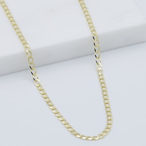 May include: A gold chain necklace with a curb link style. The chain is on a white surface.