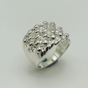 May include: A silver ring with a textured design. The ring is made of many small, round beads that are clustered together.