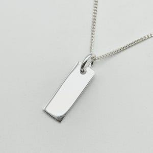 May include: A silver rectangular pendant necklace with a polished finish. The pendant hangs from a delicate silver chain. The necklace is displayed against a light background.