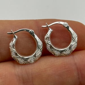 May include: A pair of silver hoop earrings with a textured, geometric design. The earrings are small and delicate.