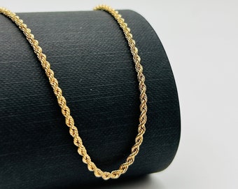 May include: A gold rope chain necklace on a black background.