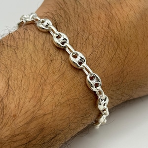 Könnte beinhalten: Ein silbernes Armband mit einem Ankerketten-Design. Das Armband befindet sich an einem Handgelenk.