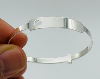 May include: A silver bangle bracelet with a heart-shaped cutout on a rectangular plate. The bracelet has a spring clasp.
