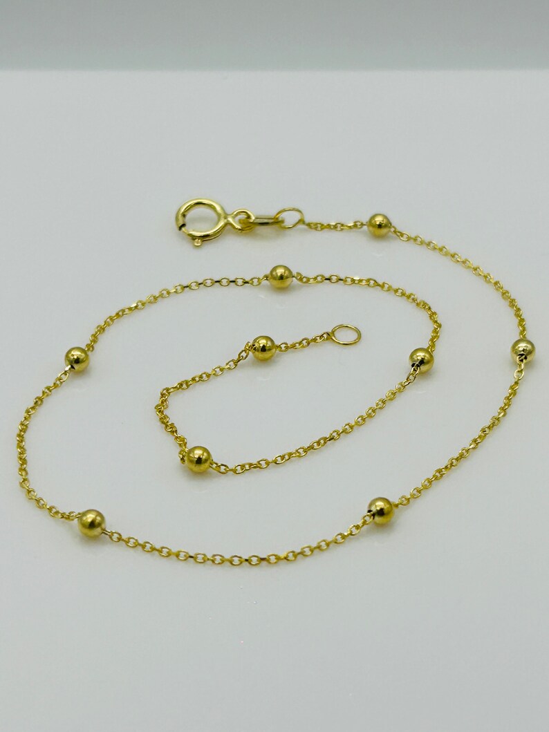 May include: A delicate gold chain anklet with small round beads. The anklet has a lobster clasp closure.