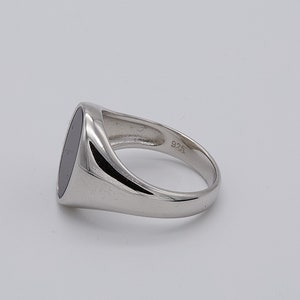 May include: A silver signet ring with a black oval stone. The ring is marked "925" on the inside band.