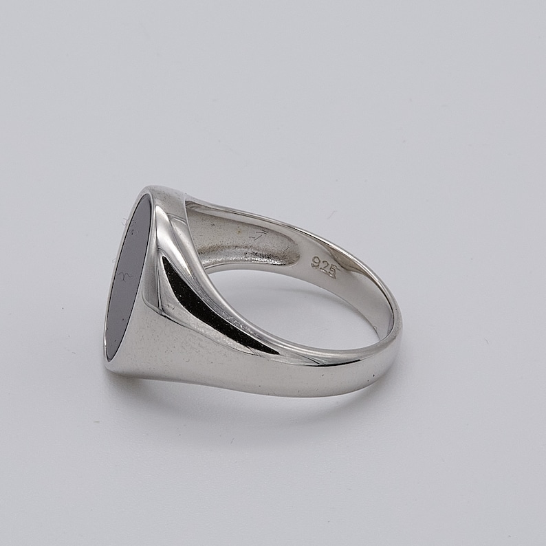 May include: A silver signet ring with a black oval stone. The ring is marked "925" on the inside band.