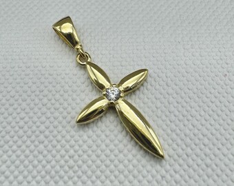 Könnte beinhalten: Ein goldfarbener Anhänger in Form eines Kreuzes. Das Kreuz hat vier längliche Blütenblätter mit einem kleinen, runden, klaren Edelstein in der Mitte. Der Anhänger hat oben eine Schlaufe für eine Kette.