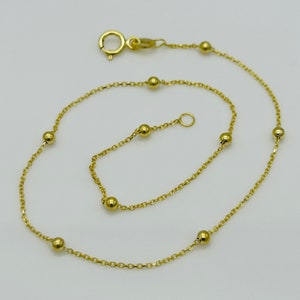 May include: A gold chain anklet with small round beads. The anklet has a lobster clasp closure.