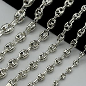 May include: Close-up of several silver-colored, polished chains with a distinctive oval-link design. The chains vary in size, showcasing the detail of the metalwork. The background is a mix of black and white.