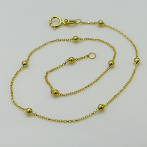 May include: A gold chain anklet with small round beads. The anklet has a lobster clasp closure.